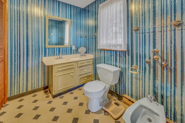 bathroom featuring wallpapered walls, baseboards, toilet, a bidet, and vanity