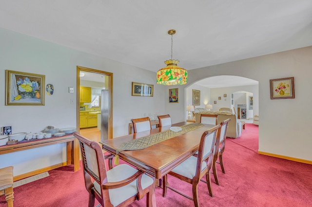 dining space with baseboards, arched walkways, and light colored carpet