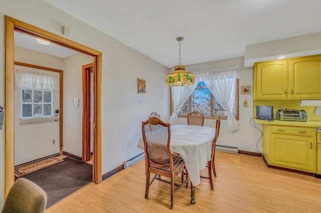 dining area featuring a baseboard heating unit, a toaster, baseboards, and light wood-type flooring