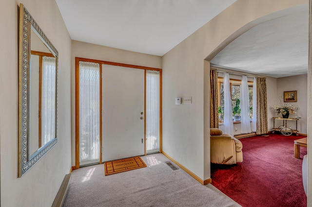 carpeted foyer with arched walkways, visible vents, and baseboards