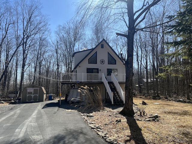 view of front of property with an outbuilding, stairway, driveway, a deck, and a storage shed