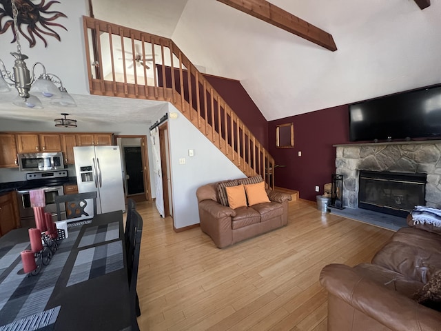 living room featuring stairway, beamed ceiling, light wood-type flooring, a fireplace, and high vaulted ceiling