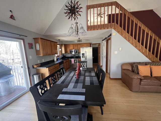 dining room with stairs, a barn door, light wood-style floors, a notable chandelier, and high vaulted ceiling