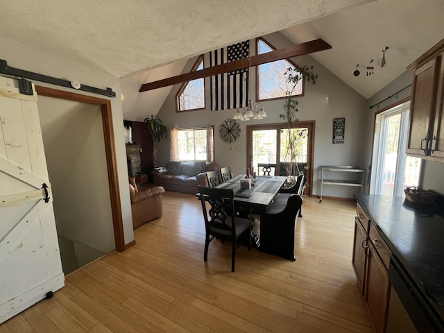 dining area featuring a barn door, a textured ceiling, light wood-style flooring, and high vaulted ceiling