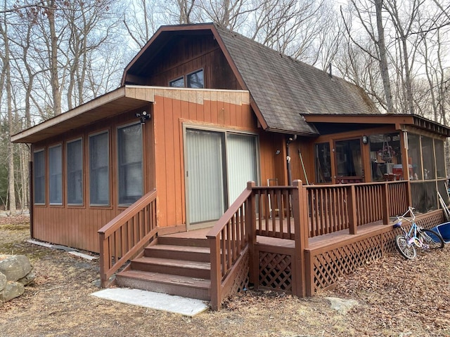 back of house with a gambrel roof, a wooden deck, roof with shingles, and a sunroom