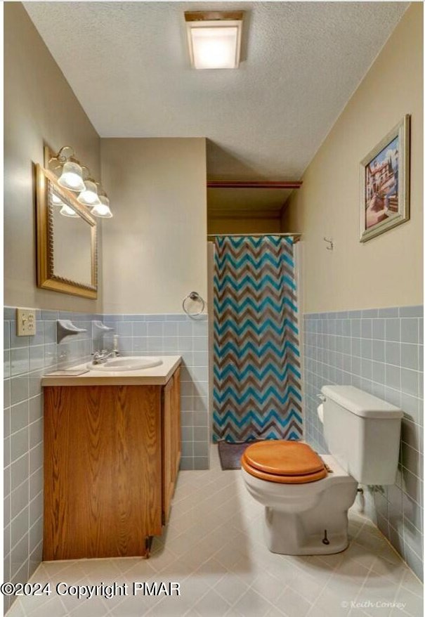 full bath with tile walls, a textured ceiling, and toilet