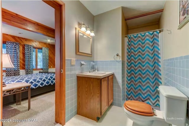 ensuite bathroom with toilet, beamed ceiling, vanity, and tile walls