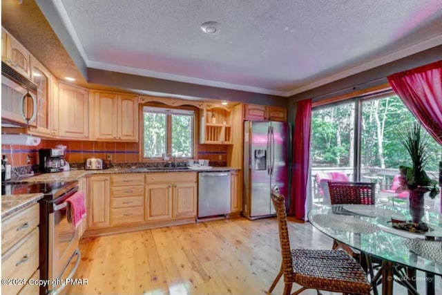 kitchen with appliances with stainless steel finishes, light brown cabinets, a sink, a textured ceiling, and light wood-type flooring