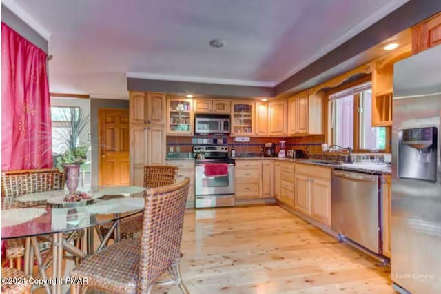 kitchen featuring dark countertops, glass insert cabinets, stainless steel appliances, light wood-type flooring, and a sink