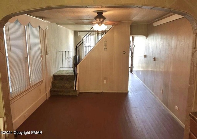 interior space featuring stairway, wooden walls, arched walkways, and a ceiling fan