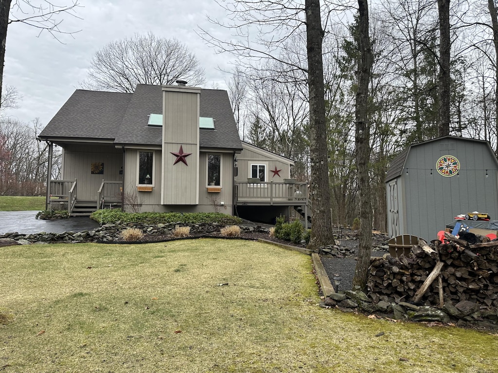 view of front of property with a front lawn, an outbuilding, a chimney, roof with shingles, and a storage unit
