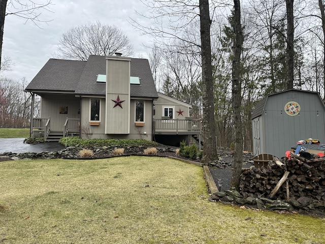 view of front of property with a front lawn, an outbuilding, a chimney, roof with shingles, and a storage unit