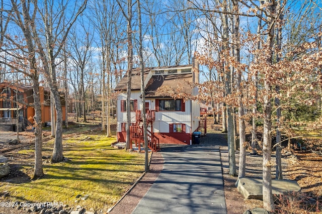 chalet / cabin featuring aphalt driveway, stairway, a front yard, and roof with shingles