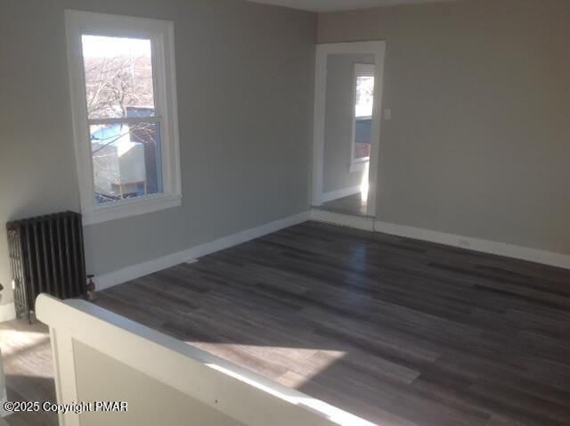 unfurnished room with radiator, a healthy amount of sunlight, baseboards, and wood finished floors