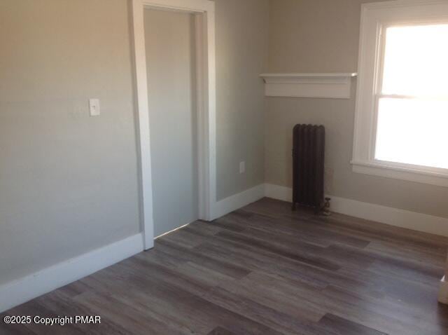 unfurnished living room with radiator heating unit, baseboards, and dark wood-style flooring