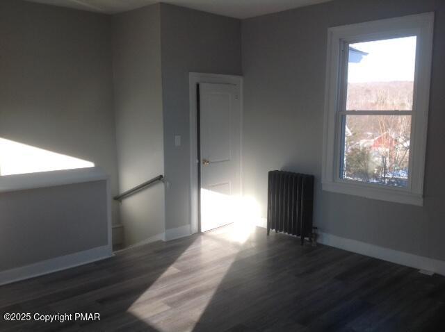 empty room with baseboards, wood finished floors, and radiator