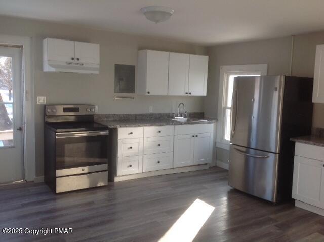 kitchen with sink, dark stone counters, dark hardwood / wood-style flooring, stainless steel appliances, and white cabinets