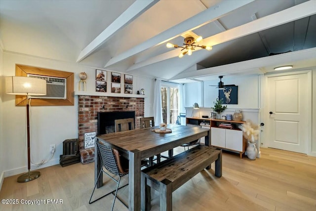 dining area featuring lofted ceiling with beams, a wall mounted AC, a brick fireplace, light wood-type flooring, and ceiling fan with notable chandelier