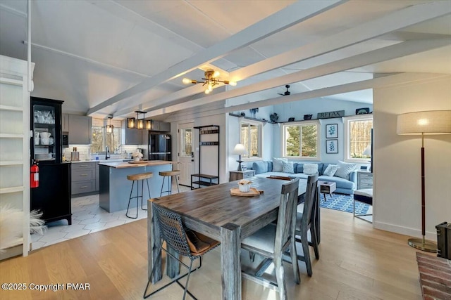 dining space with baseboards, light wood finished floors, beam ceiling, and a notable chandelier