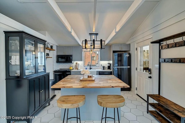 kitchen featuring black appliances, wood counters, a breakfast bar area, and a wealth of natural light