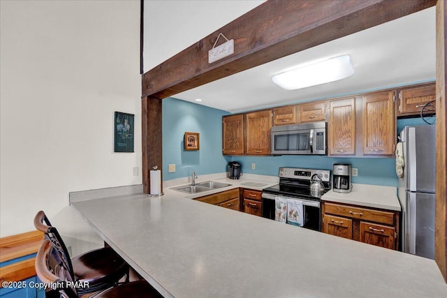 kitchen featuring brown cabinets, appliances with stainless steel finishes, a kitchen breakfast bar, and a sink