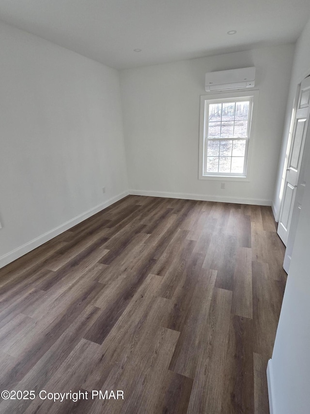 spare room with a wall mounted AC, baseboards, and dark wood-style flooring