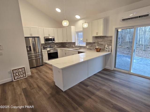 kitchen featuring a peninsula, a sink, an AC wall unit, white cabinets, and appliances with stainless steel finishes