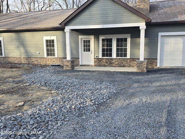 view of front of house featuring stone siding, covered porch, roof with shingles, and a chimney