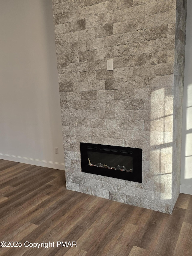 details featuring a stone fireplace, baseboards, and wood finished floors