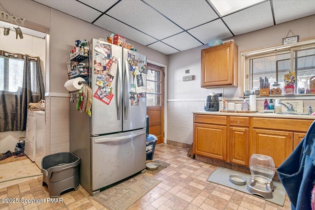 kitchen featuring a drop ceiling, a wainscoted wall, tile walls, light countertops, and freestanding refrigerator