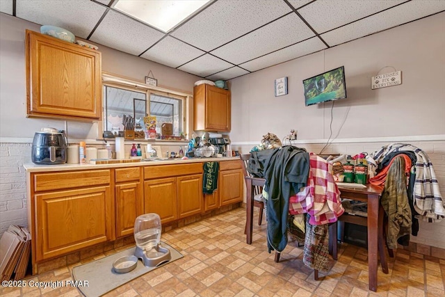 kitchen with a paneled ceiling, a wainscoted wall, light countertops, and a sink