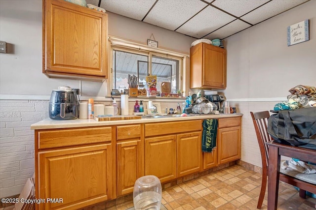 kitchen with a wainscoted wall, light countertops, and a drop ceiling