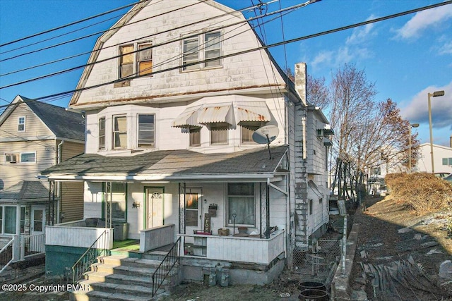 view of front facade featuring a chimney, a porch, and a gambrel roof