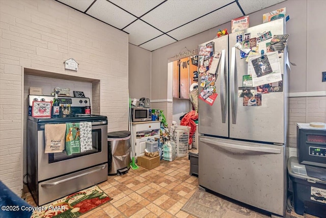 kitchen with stainless steel appliances, brick floor, and a drop ceiling