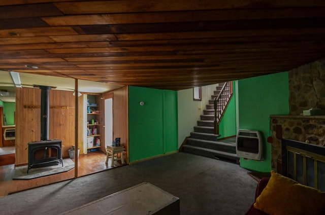 finished basement featuring a fireplace, heating unit, stairway, a wood stove, and carpet flooring