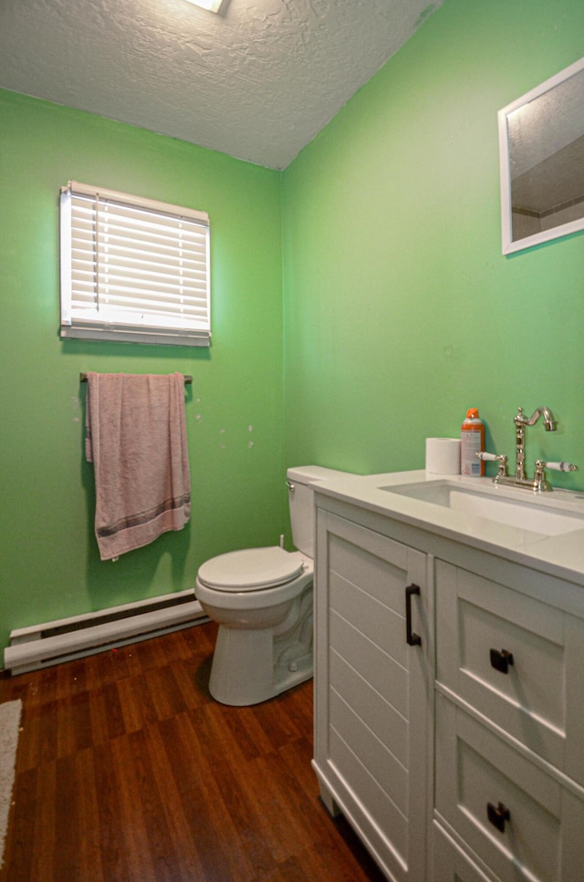 half bathroom with a baseboard radiator, toilet, a textured ceiling, vanity, and wood finished floors