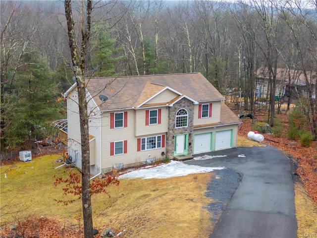 traditional home featuring aphalt driveway, a garage, stone siding, a front lawn, and a view of trees