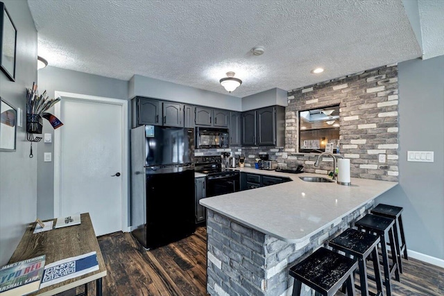 kitchen featuring dark wood-style floors, a kitchen breakfast bar, a peninsula, black appliances, and a sink