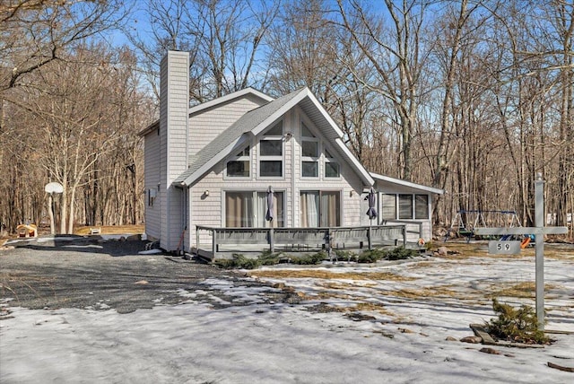 chalet / cabin with driveway, a sunroom, a chimney, and a deck