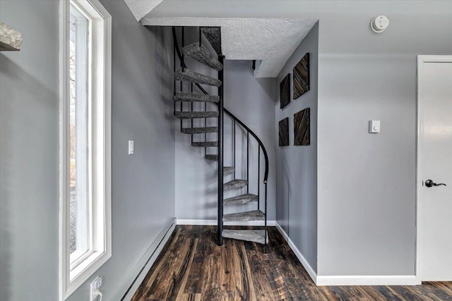 stairs with a baseboard heating unit, a textured ceiling, baseboards, and wood finished floors