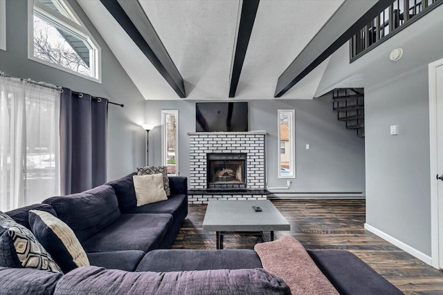 living area with a textured ceiling, wood finished floors, baseboards, a brick fireplace, and beam ceiling