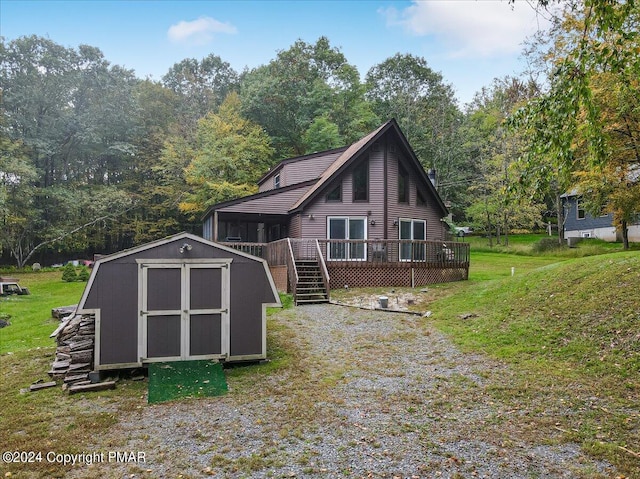 back of house with a wooded view, a shed, a wooden deck, a lawn, and an outdoor structure