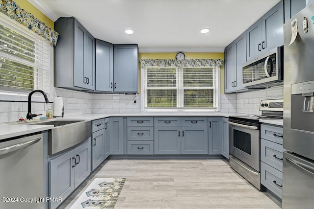 kitchen featuring light wood finished floors, light countertops, decorative backsplash, appliances with stainless steel finishes, and a sink