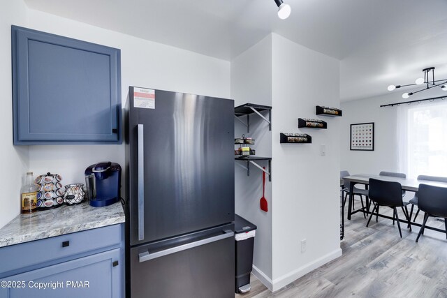 kitchen featuring light stone counters, freestanding refrigerator, light wood-style flooring, and baseboards