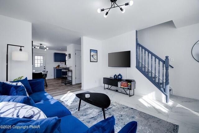 living room featuring marble finish floor, a notable chandelier, baseboards, and stairs