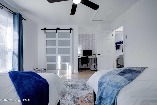 bedroom with ceiling fan, a barn door, wood finished floors, and attic access