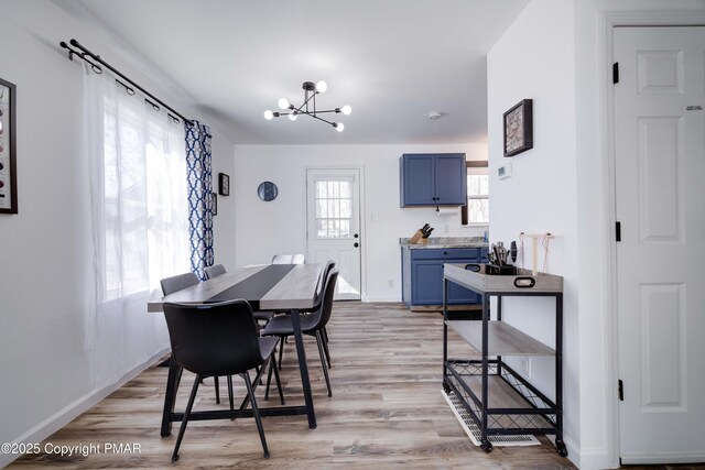 dining area with light wood-style flooring, baseboards, and a notable chandelier