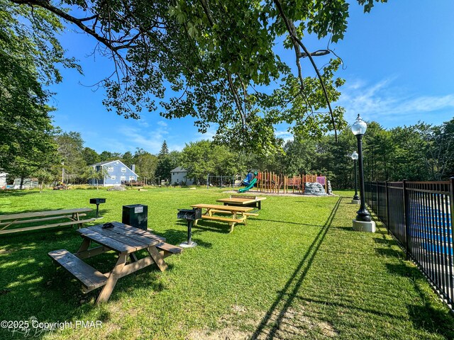 view of community featuring playground community, a yard, and fence