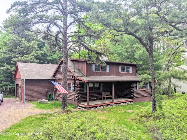 view of front of property featuring a front lawn, covered porch, log exterior, and driveway