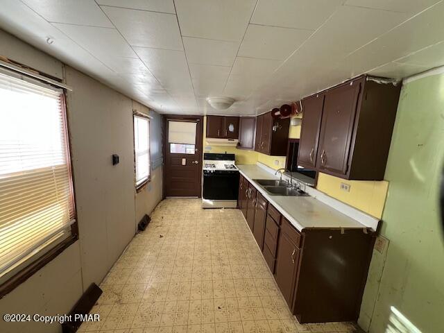 kitchen featuring gas stove, light countertops, a sink, and dark brown cabinets